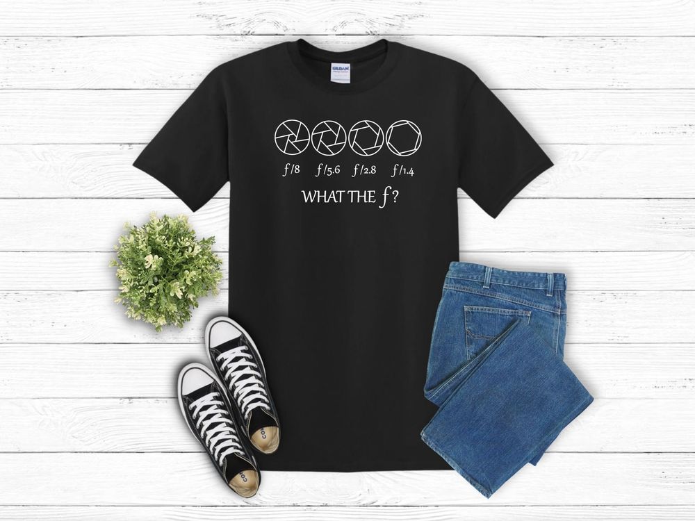 Black t-shirt with anime expressions design laid flat with blue jeans and black sneakers against white wooden background.