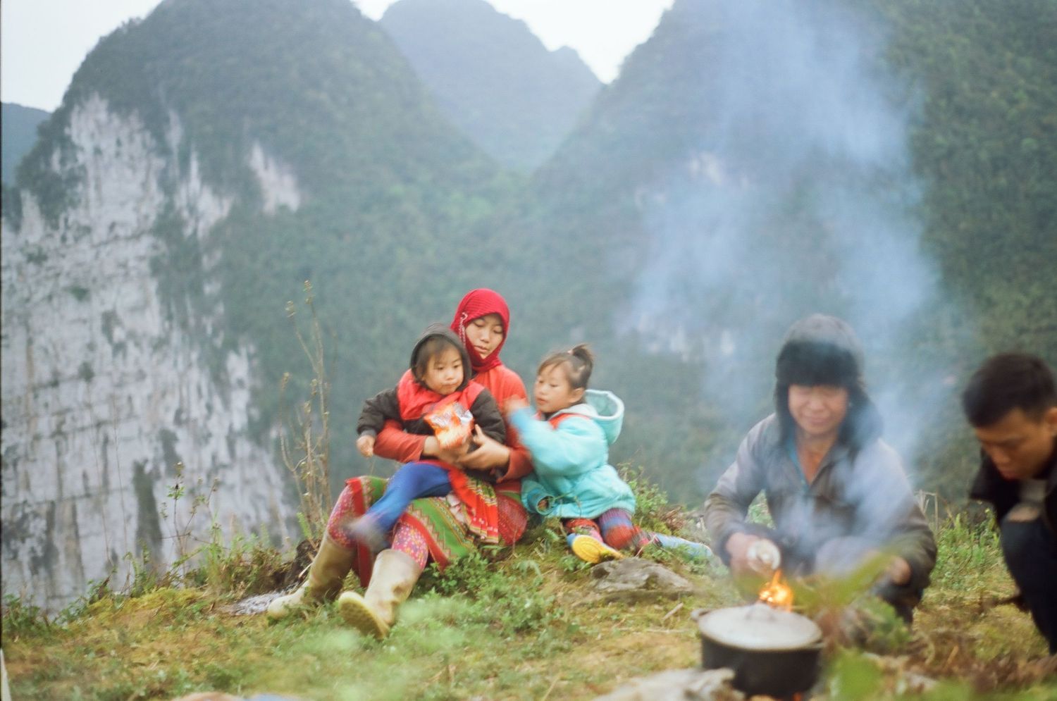 People gathered around a campfire in a misty mountain valley setting.
