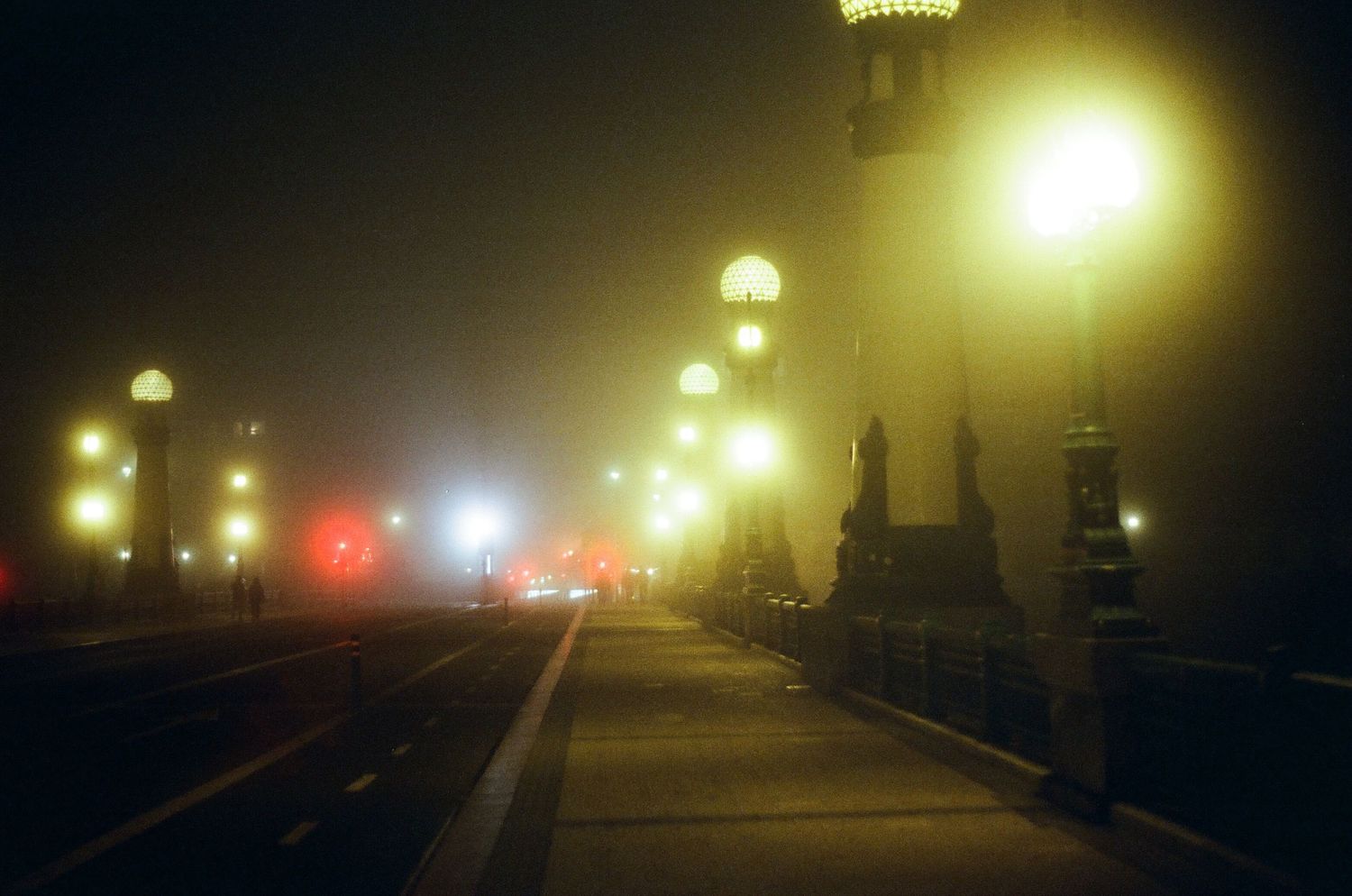 Foggy night view of illuminated bridge with glowing lampposts.