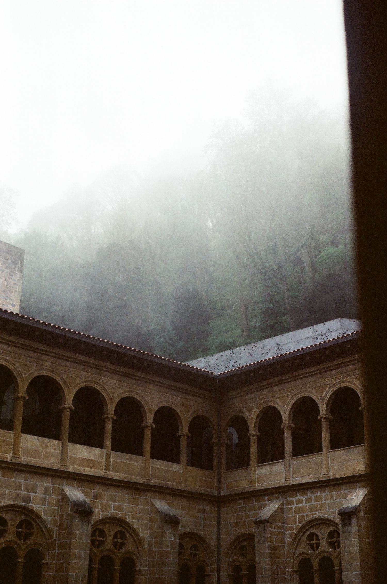 Stone courtyard with arched colonnade surrounded by mist.