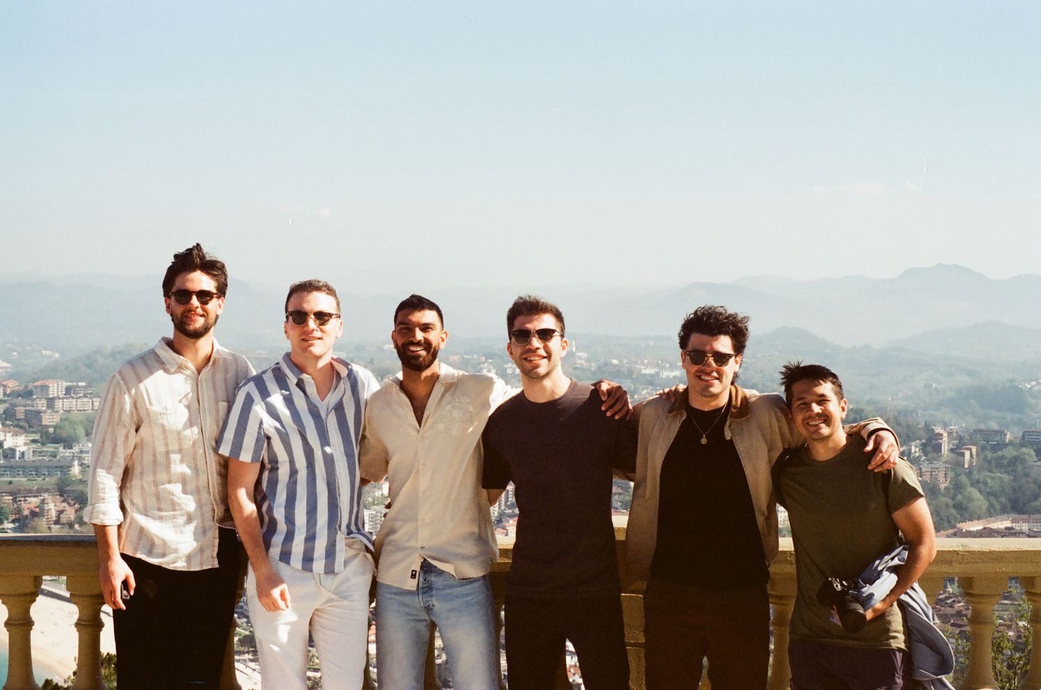 Group of friends posing together against a scenic mountain backdrop on a sunny day.