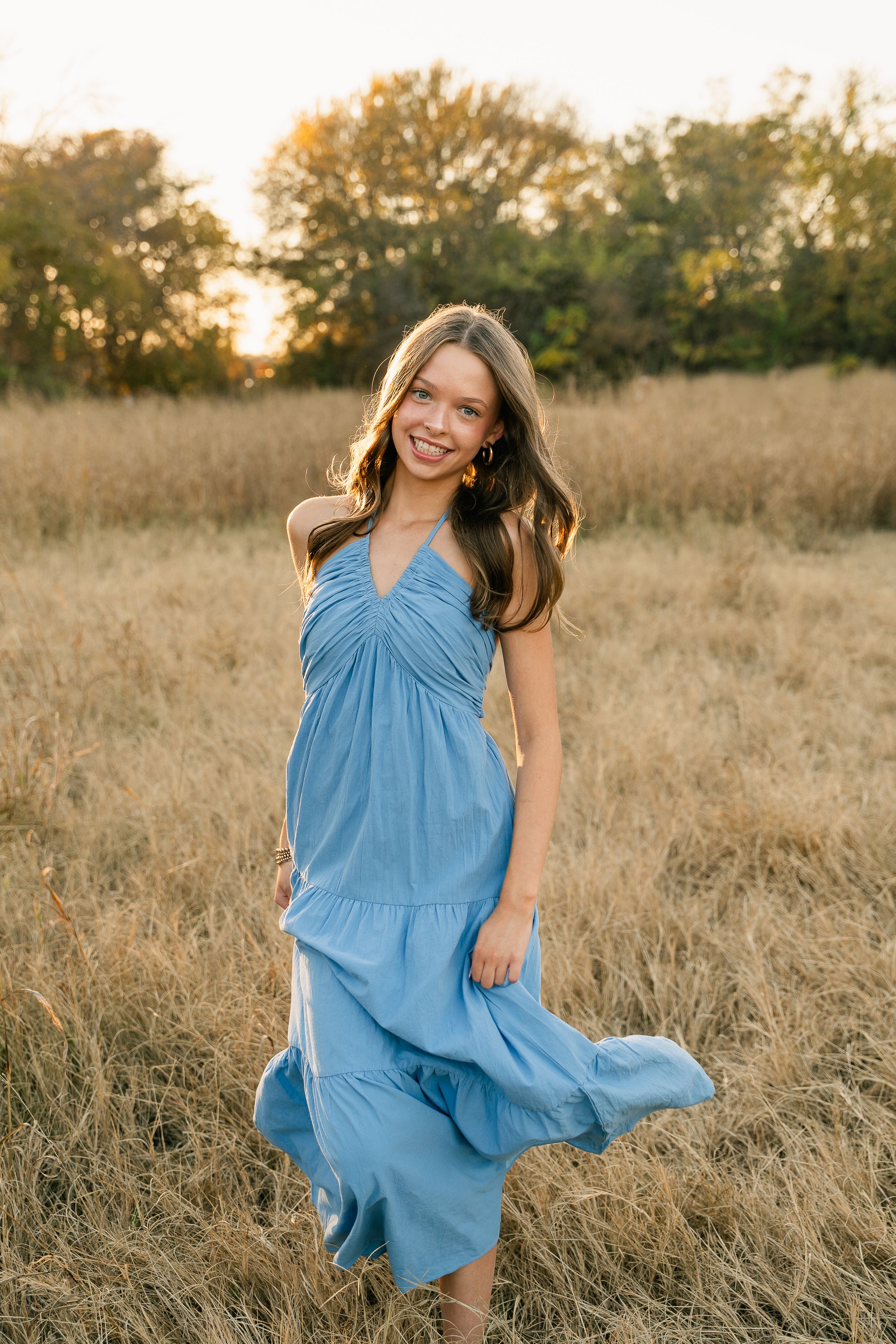 Senior session in Keller, Texas. Girl in a bright blue dress walks toward the camera while smiling in a golden field.