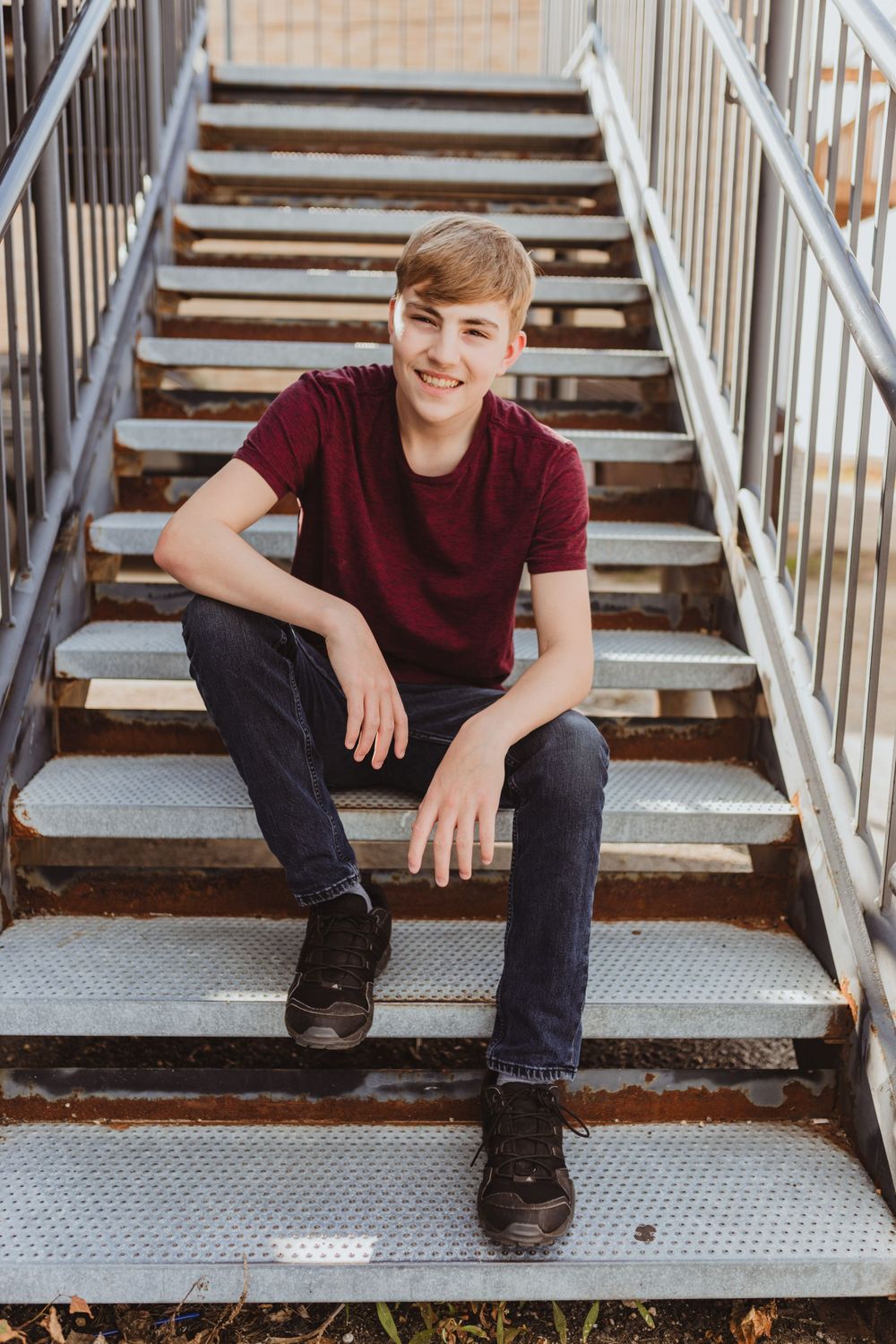 Young person sits casually on metal stairs in a relaxed outdoor portrait series.