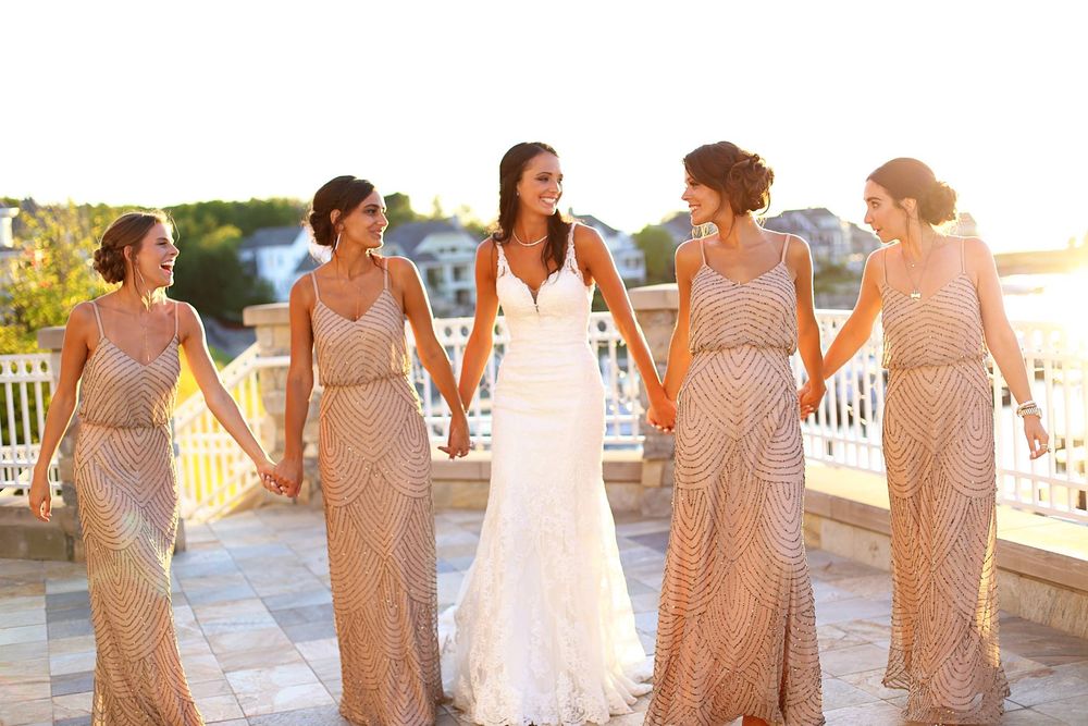 A group of bridesmaids in blush pink sequined dresses pose together at a wedding venue during golden hour at the Bay Harbor Yacht Club