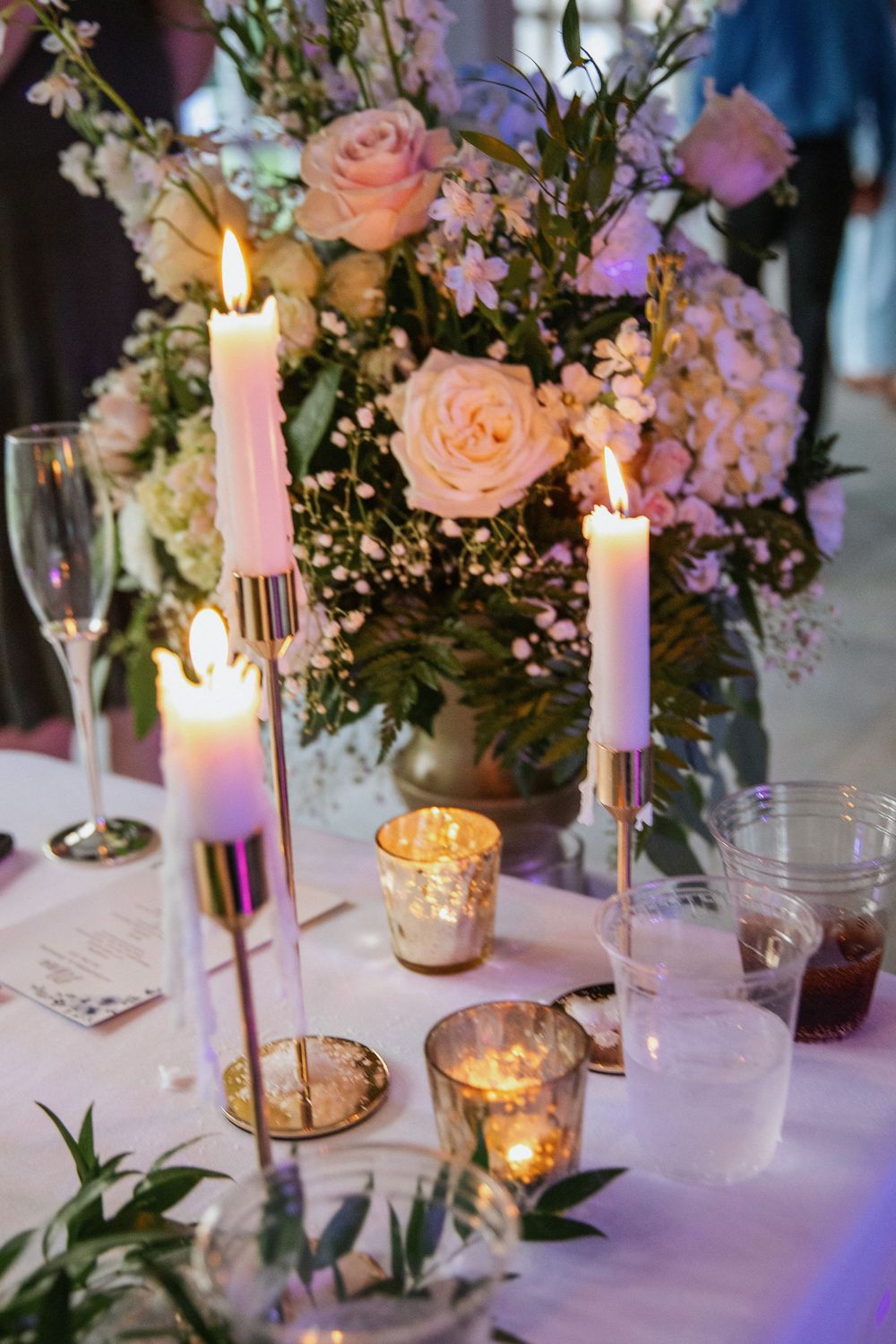 Elegant wedding table setting with pink roses, white candles, and greenery creating a romantic atmosphere.