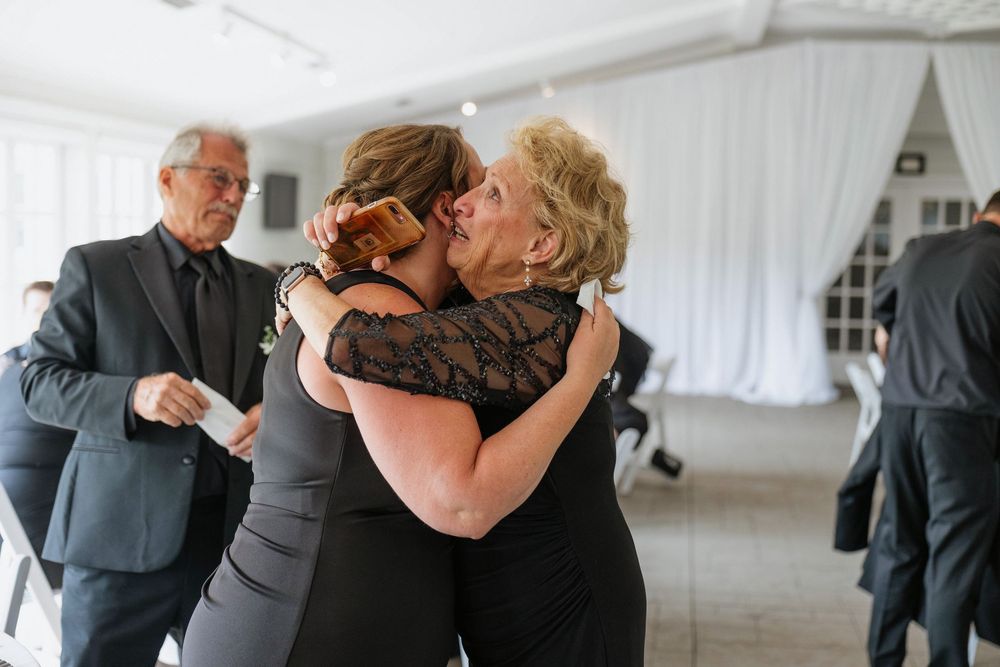 Emotional guests embrace during a wedding reception in a white tent.