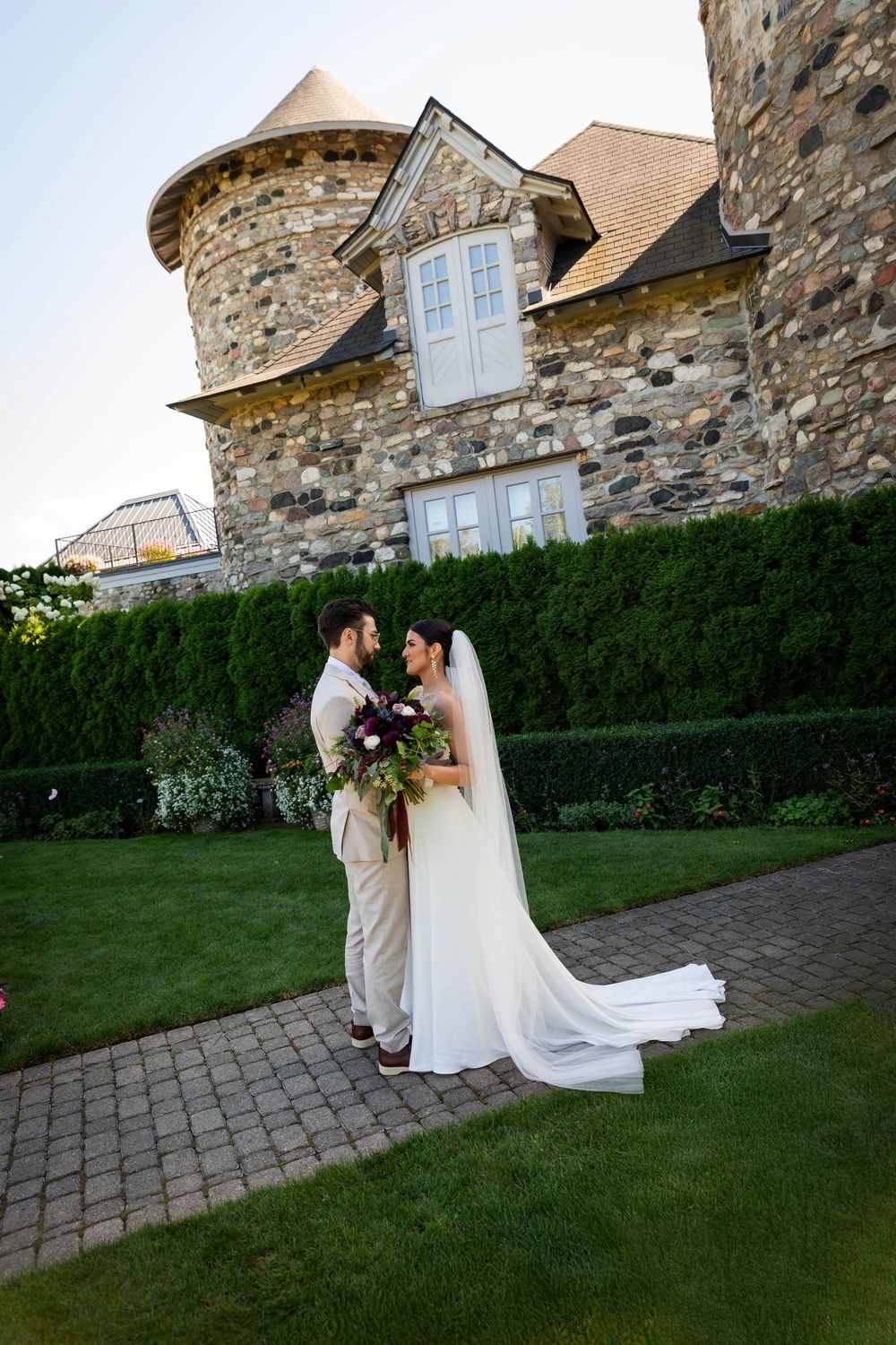 A romantic wedding couple by stone patio of a grand estate with manicured hedges at Cadtle Farms in Charlevoix Michigan