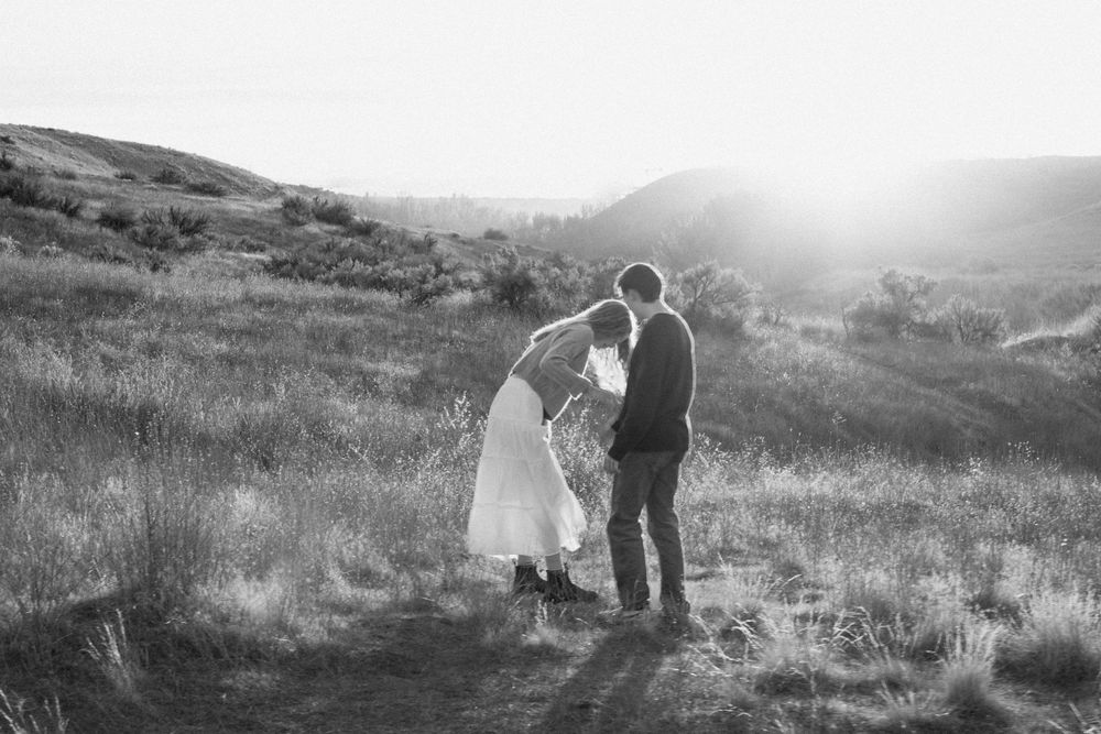 Silhouetted figures stand on a grassy hillside during sunset, creating a peaceful outdoor scene in nature.