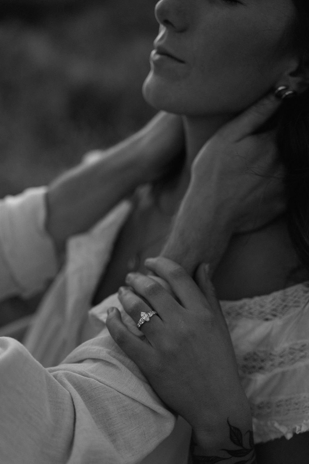 Black and white close-up of a person's neck and jawline with a delicate hand gesture showing an elegant ring.