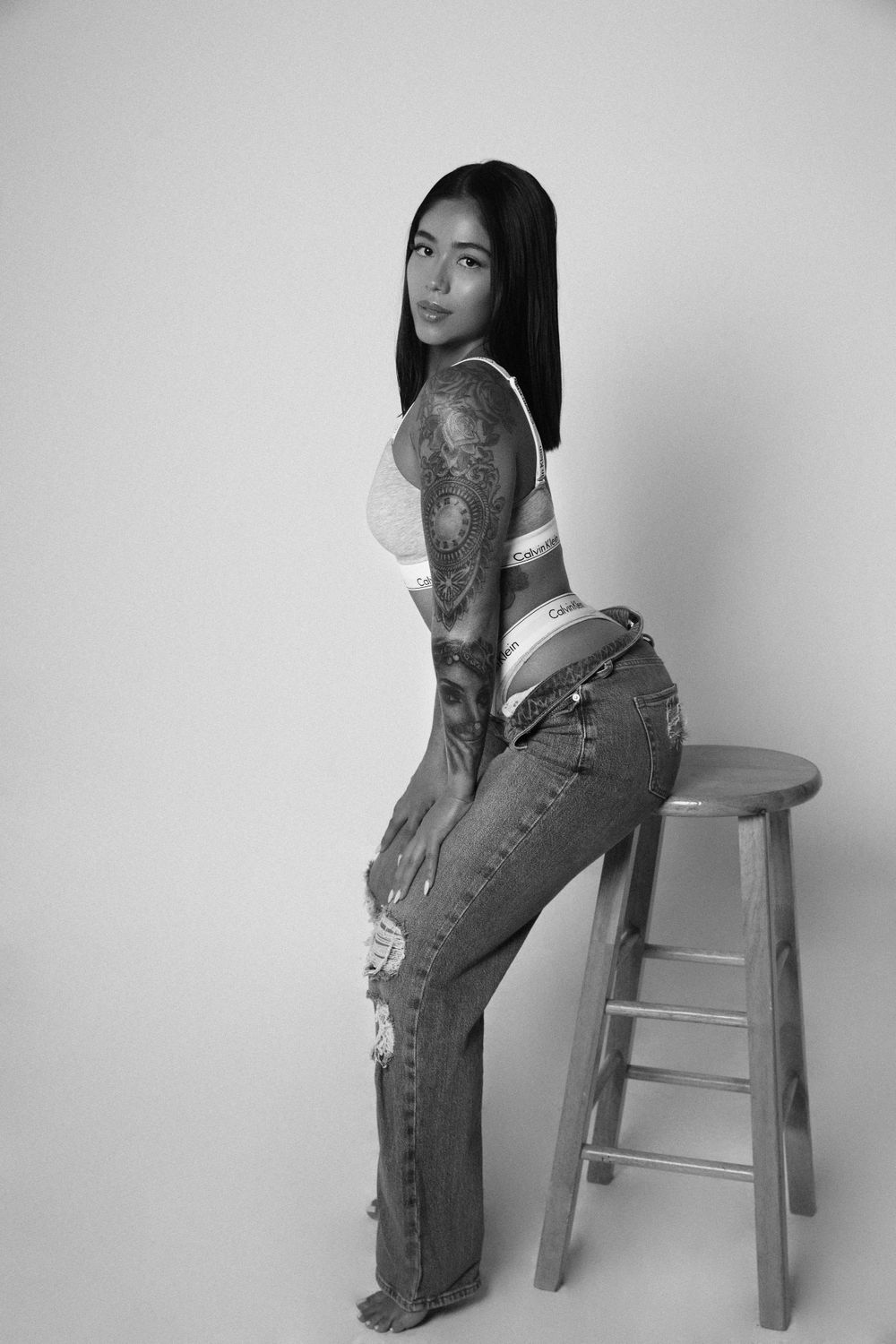 Black and white portrait of model in casual outfit posing with wooden stool.