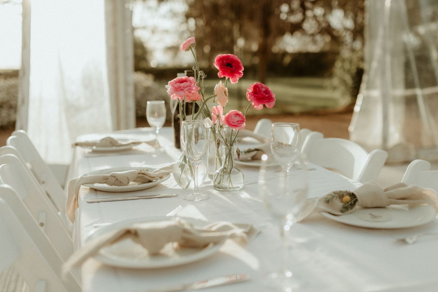 Elegant table setting with pink poppies in glass vases and white dishware for a romantic dining experience.