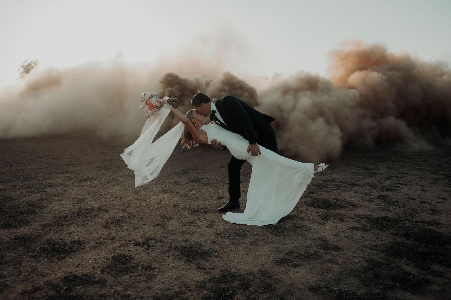 A dramatic silhouette against swirling smoke stands in a field with flowing white fabric billowing in the wind.