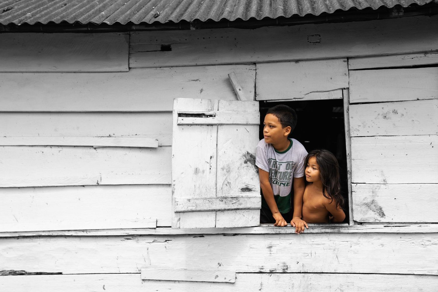 Enfant à la fenêtre d'une maison en bois, photographie en noir et blanc