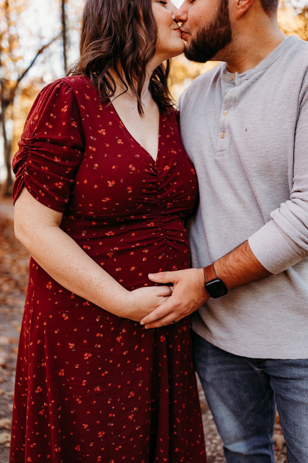 A couple standing each other and they are both holding each others hand on the expectant mothers belly.