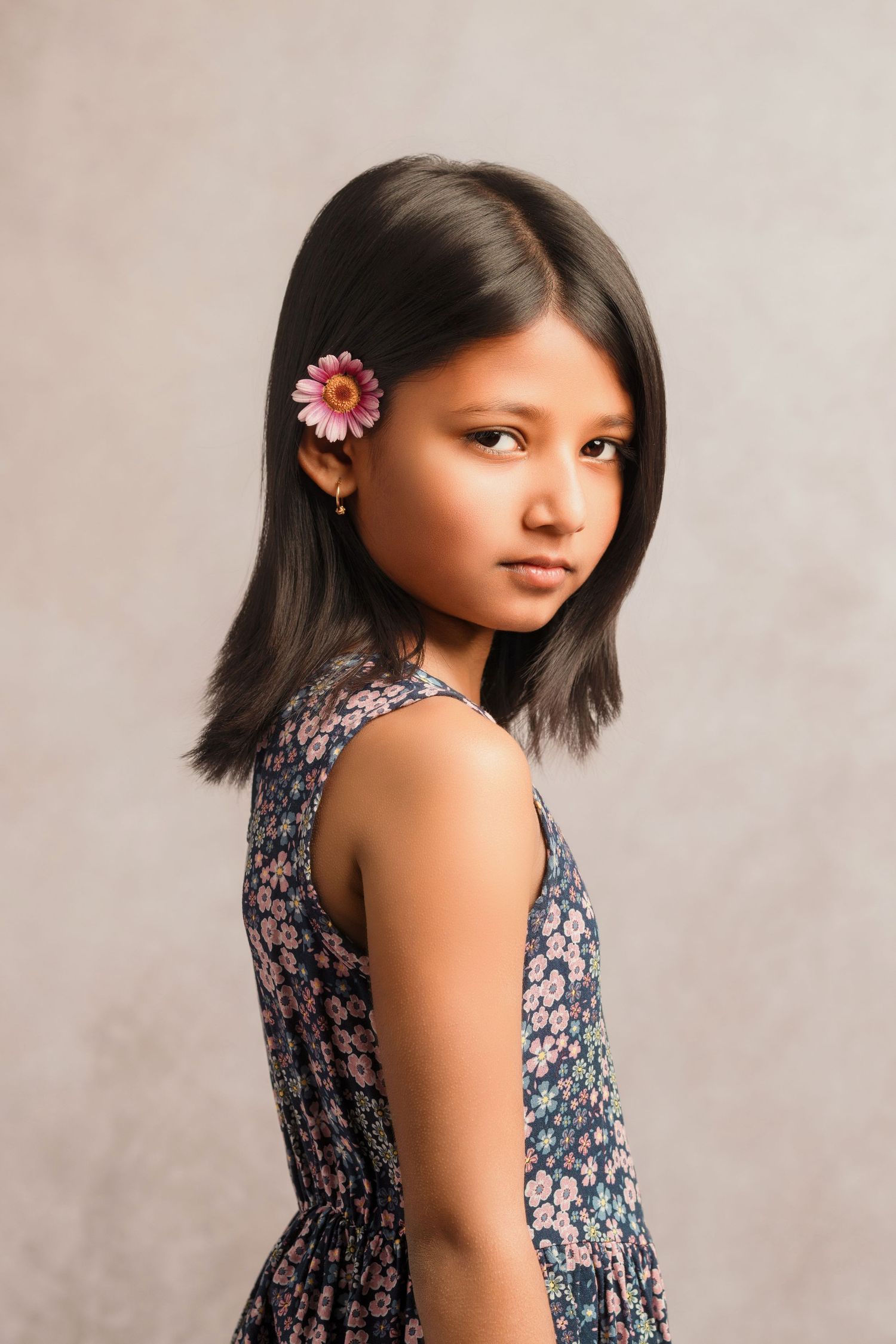 Portrait of person in a floral sundress with long dark hair and pink flower earring against neutral background.