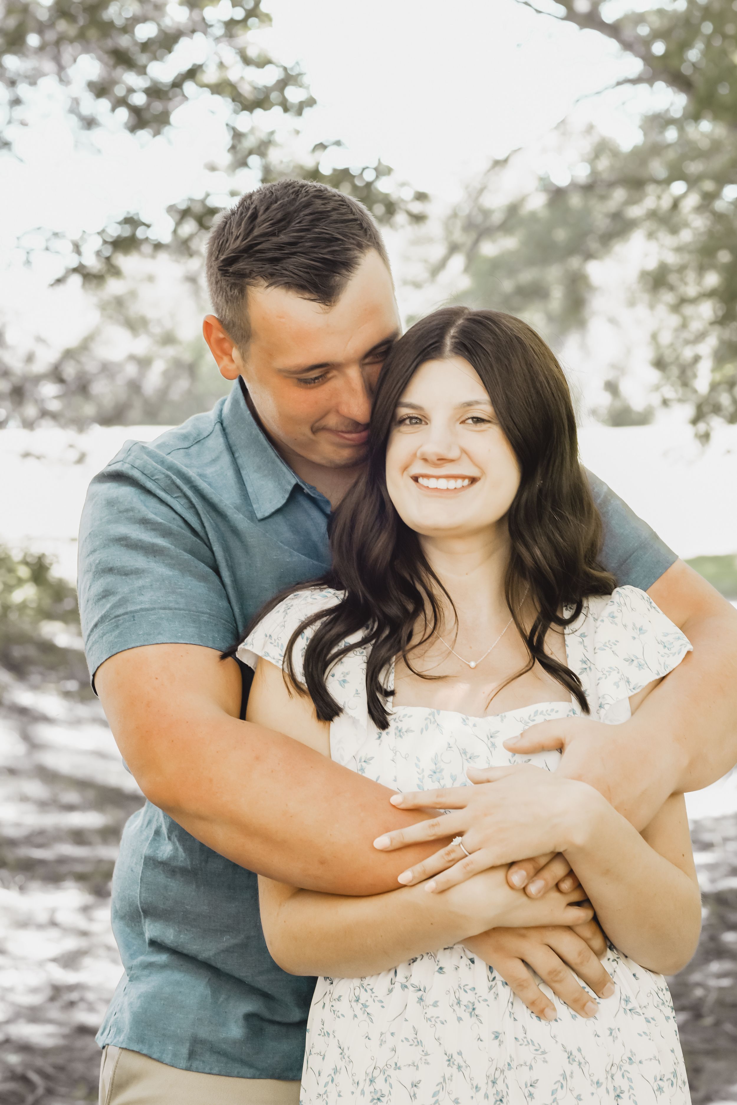 Romantic couple embraces in a sunlit outdoor setting with soft bokeh background.