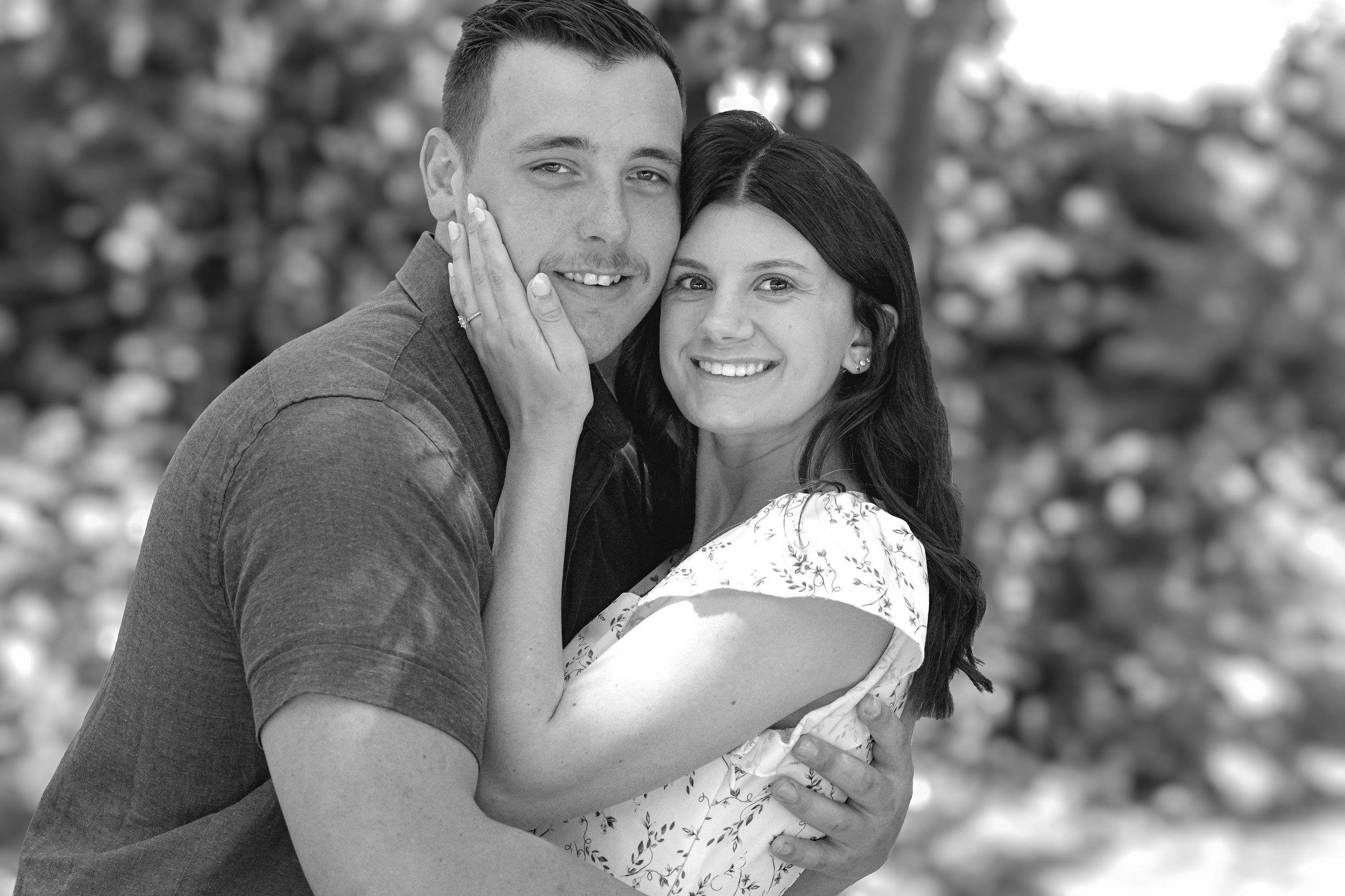 Black and white portrait of couple sharing tender moment in natural setting.