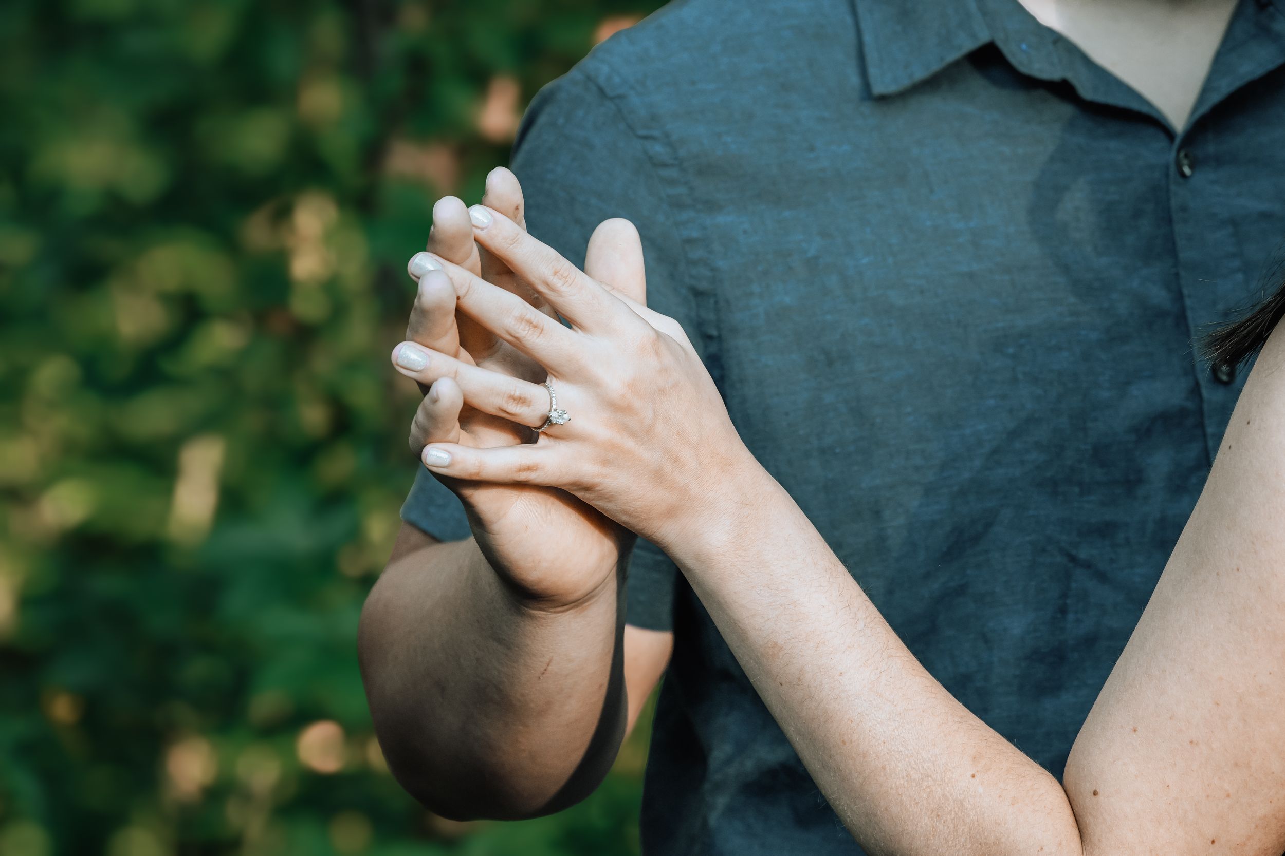 Close-up of hands displaying engagement ring in natural outdoor lighting.