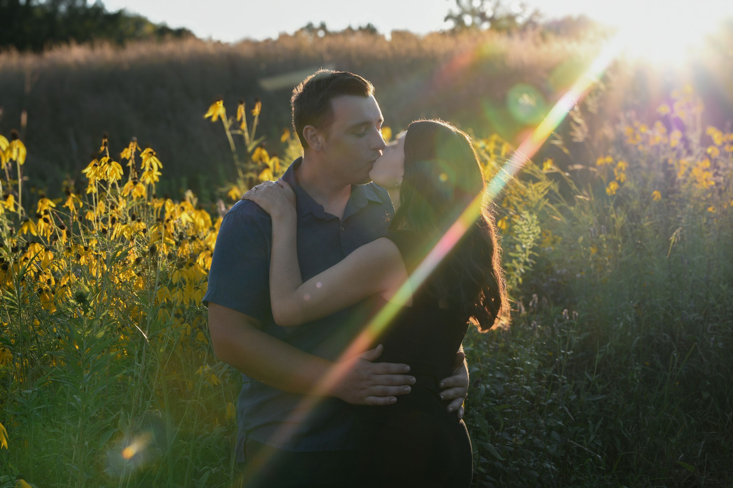 Silhouettes of a couple embracing with sunflare and yellow wildflowers in the background.