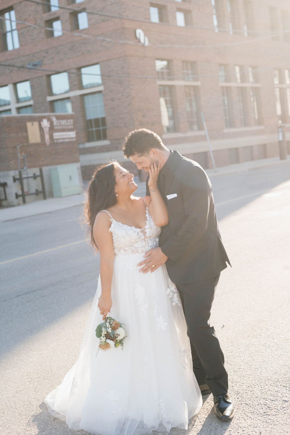 A wedding couple shares a romantic moment on a sunny urban street.