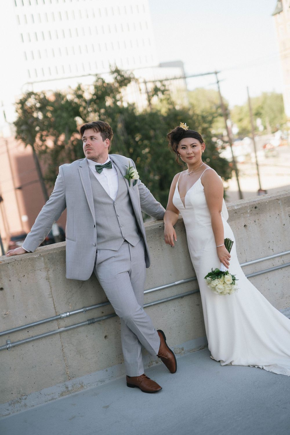 Stylish wedding couple posing against an urban concrete wall in formal attire.