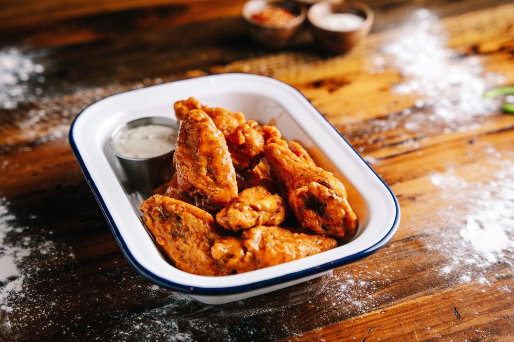 Crispy buffalo chicken wings served in a white enamel dish with creamy dipping sauce on a rustic wooden table.