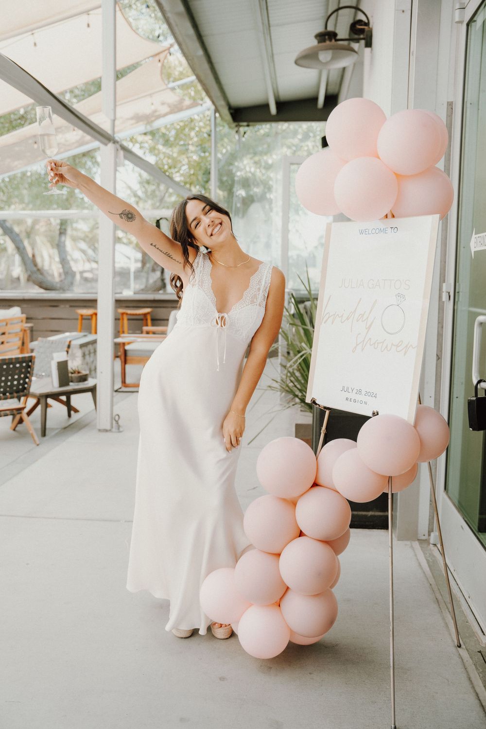 A white dress worn with pink balloon decorations and a standing sign in a bright indoor venue.