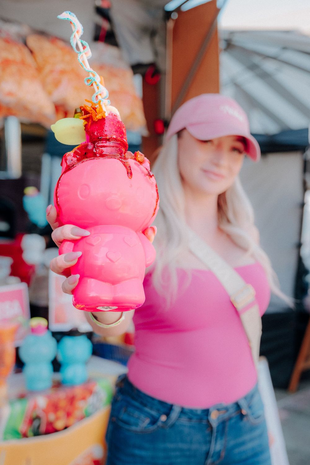 A bright pink cotton candy dessert being held up at a carnival or fair concession stand.
