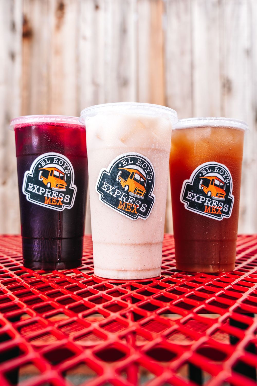 Three colorful beverages in clear plastic cups with a Silver Line Express logo on a red outdoor table surface.