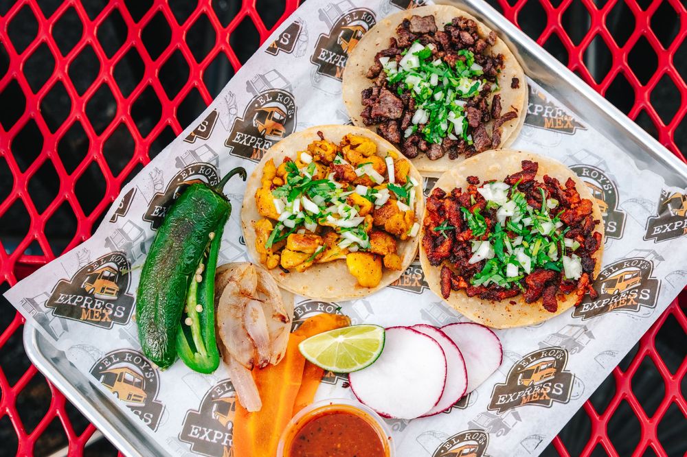 Overhead view of three Mexican street tacos with cilantro garnish, served with radishes, jalapeno and lime on wax paper.