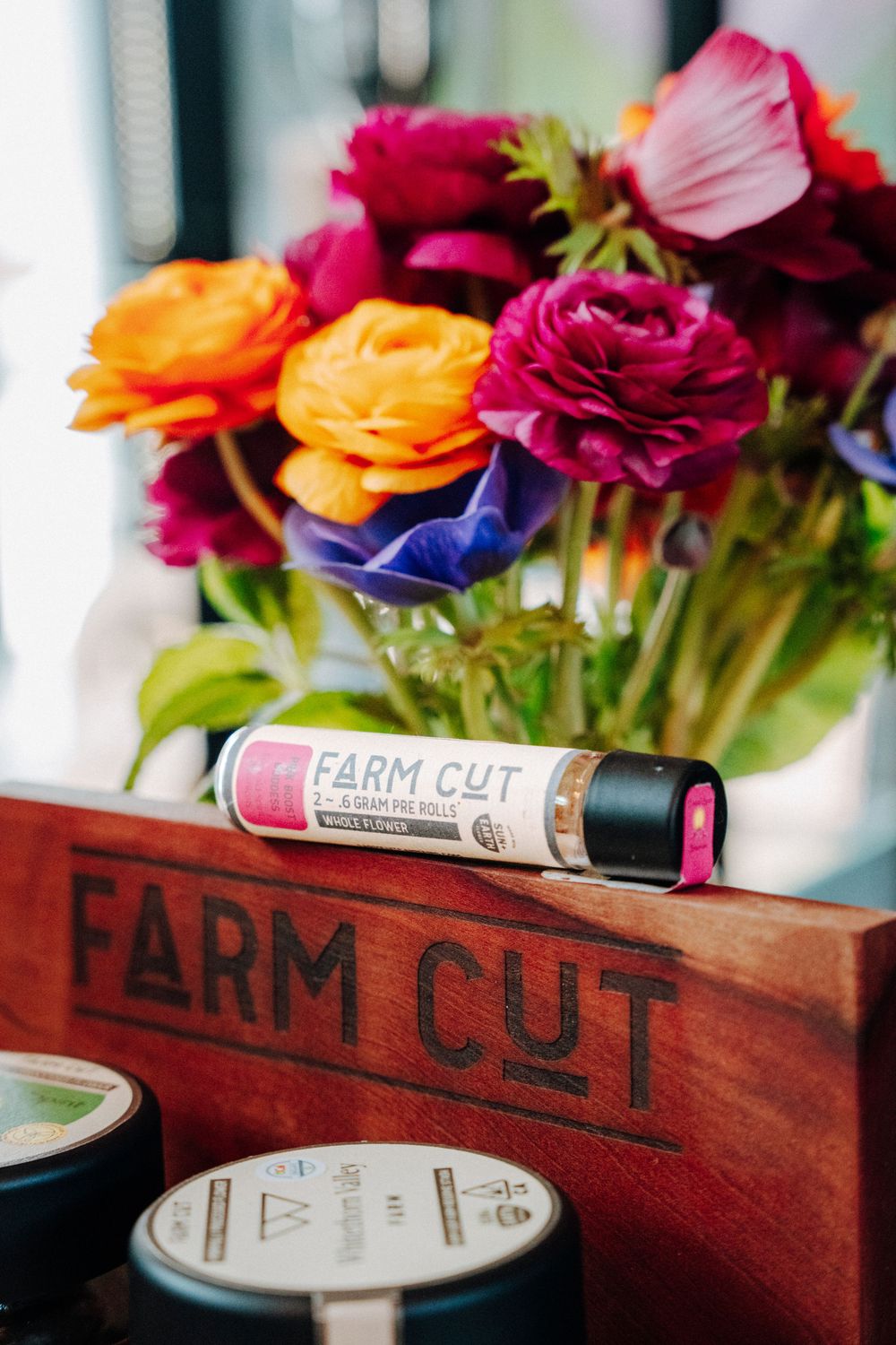 Vibrant bouquet of orange, burgundy, and blue flowers arranged in a wooden Farm Cut branded container with product tubes.