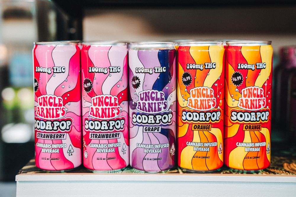 Five colorful cans of Flying Embers hard soda pop lined up displaying different flavor varieties in pink and orange tones.