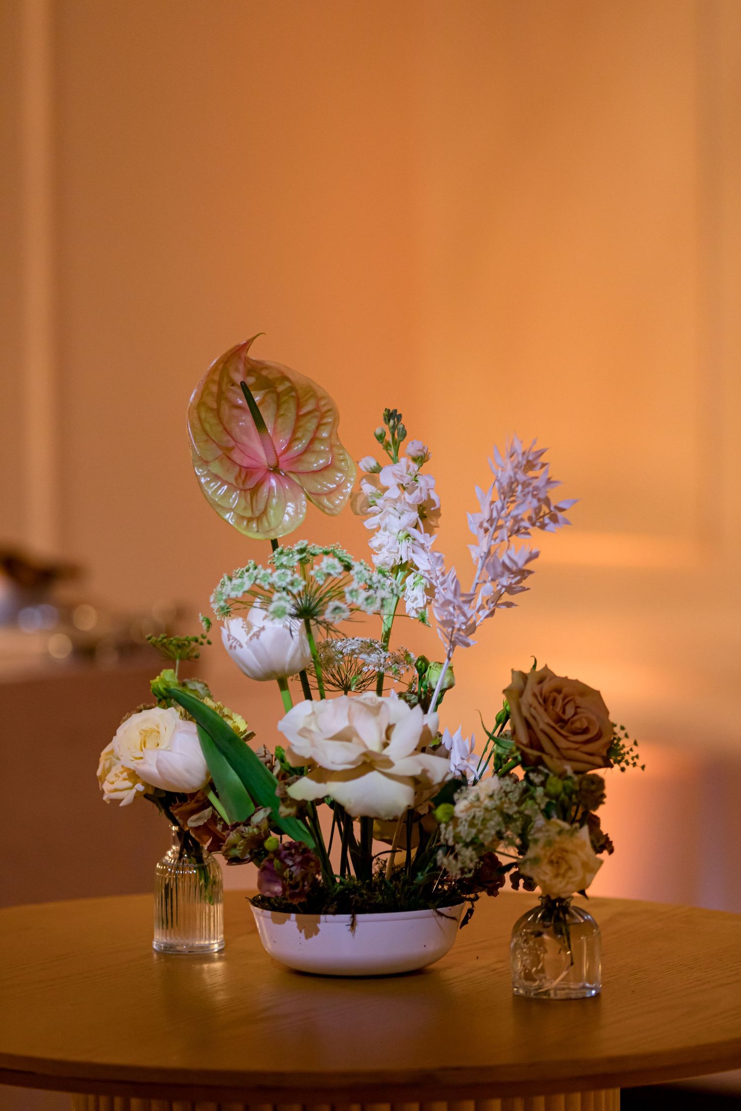 Small floral centerpieces with white and pink flowers arranged in delicate vases on a wooden table with warm lighting.