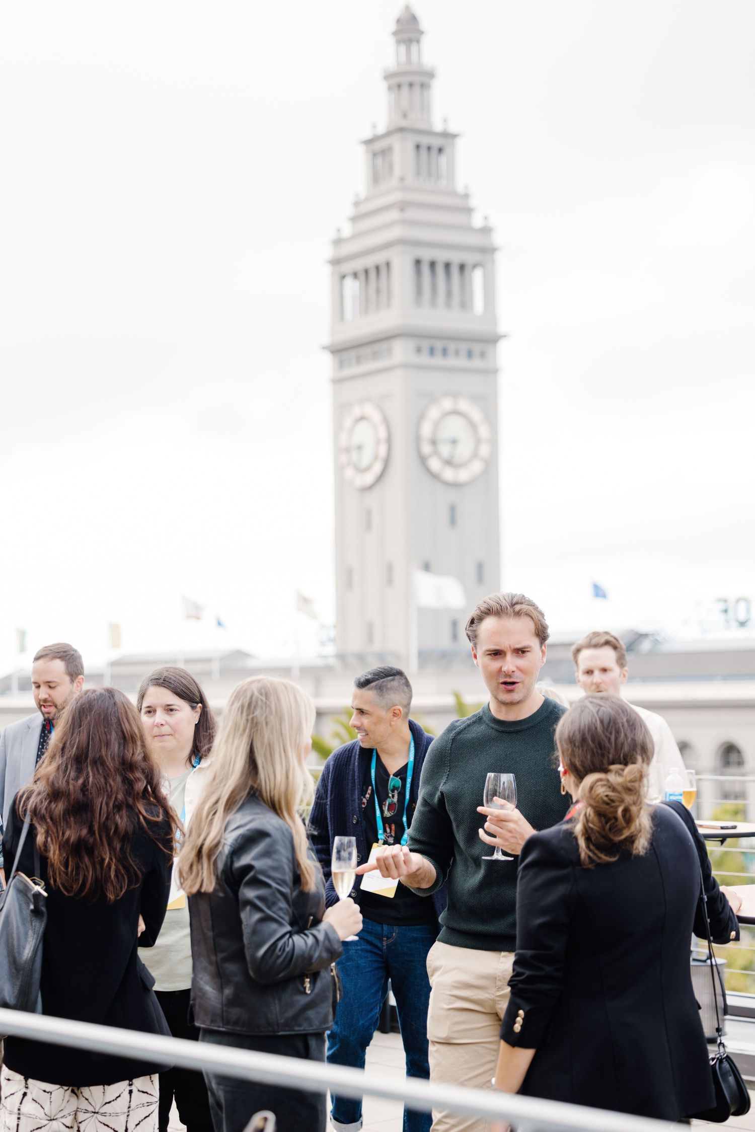 A group of people gathered on a deck or platform with white clock towers visible in the background.