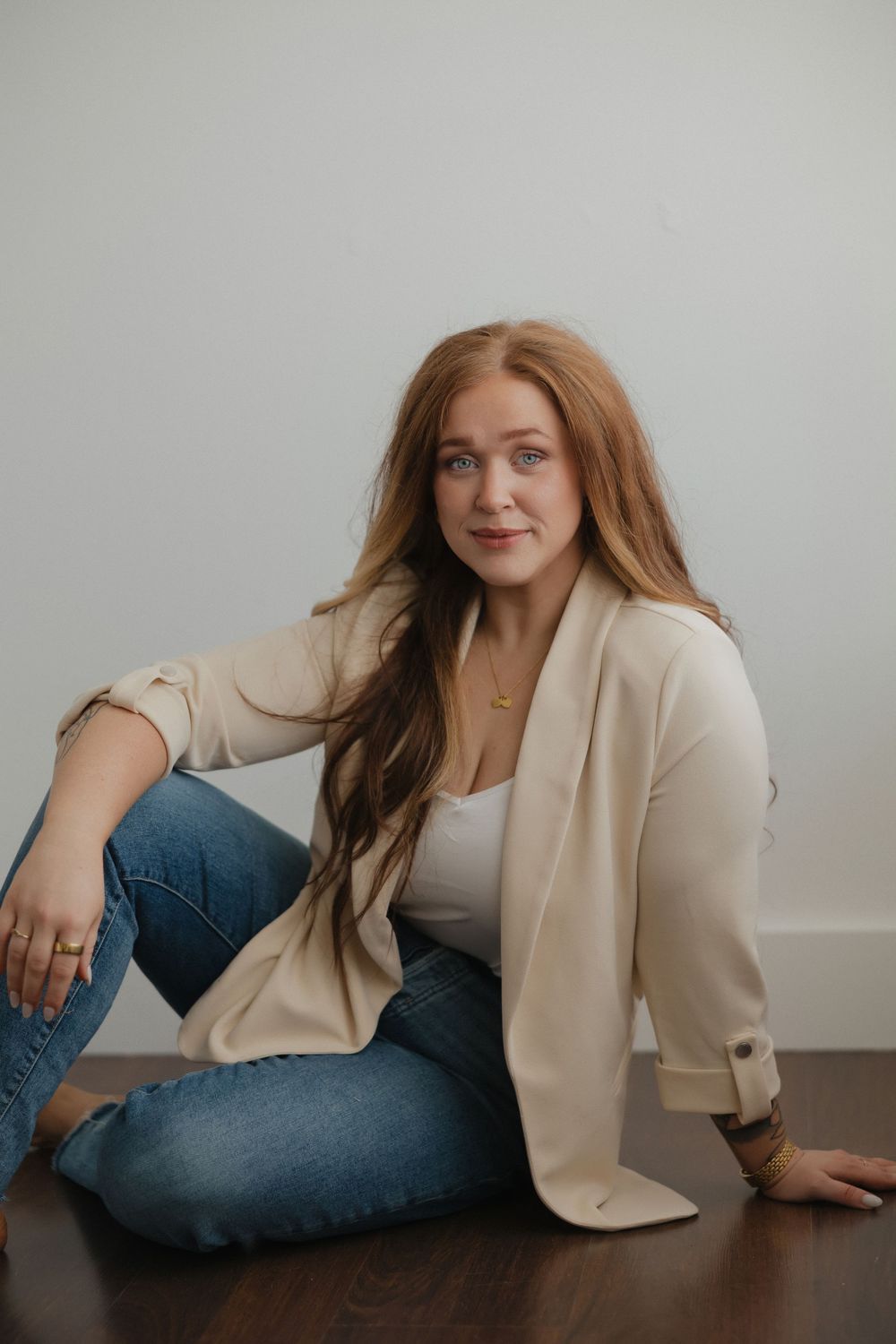 A person in a beige blazer and blue jeans strikes various reclining poses on a wooden floor against a light background.