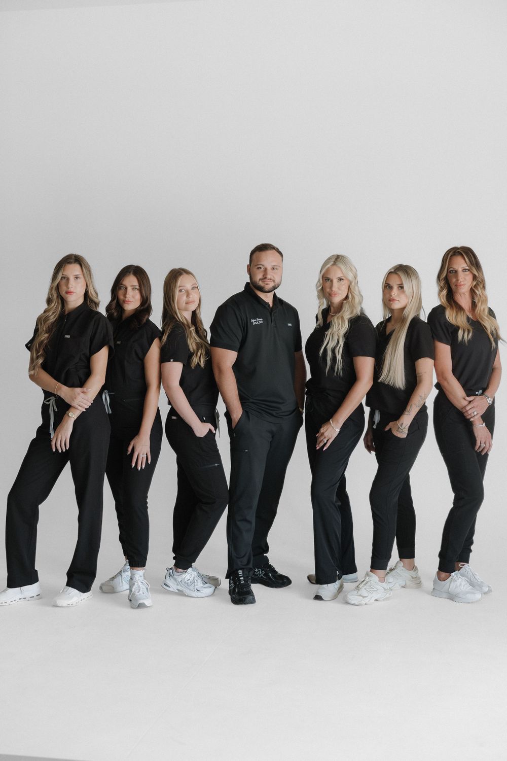 A professional medical team of seven in matching black scrubs poses confidently against a white studio background.