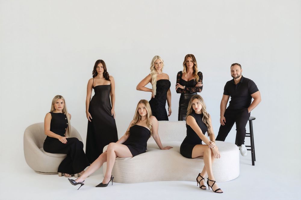 Seven people in black outfits pose elegantly in a bright studio, featuring long gowns and stylish separates.