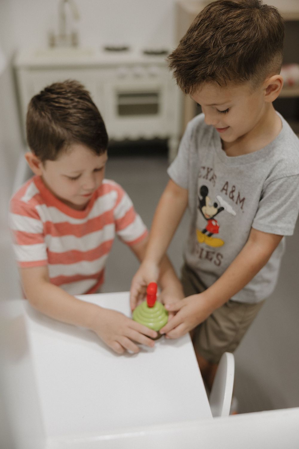 Two young boys playing with a spinning top toy in a kitchen, wearing casual shirts.