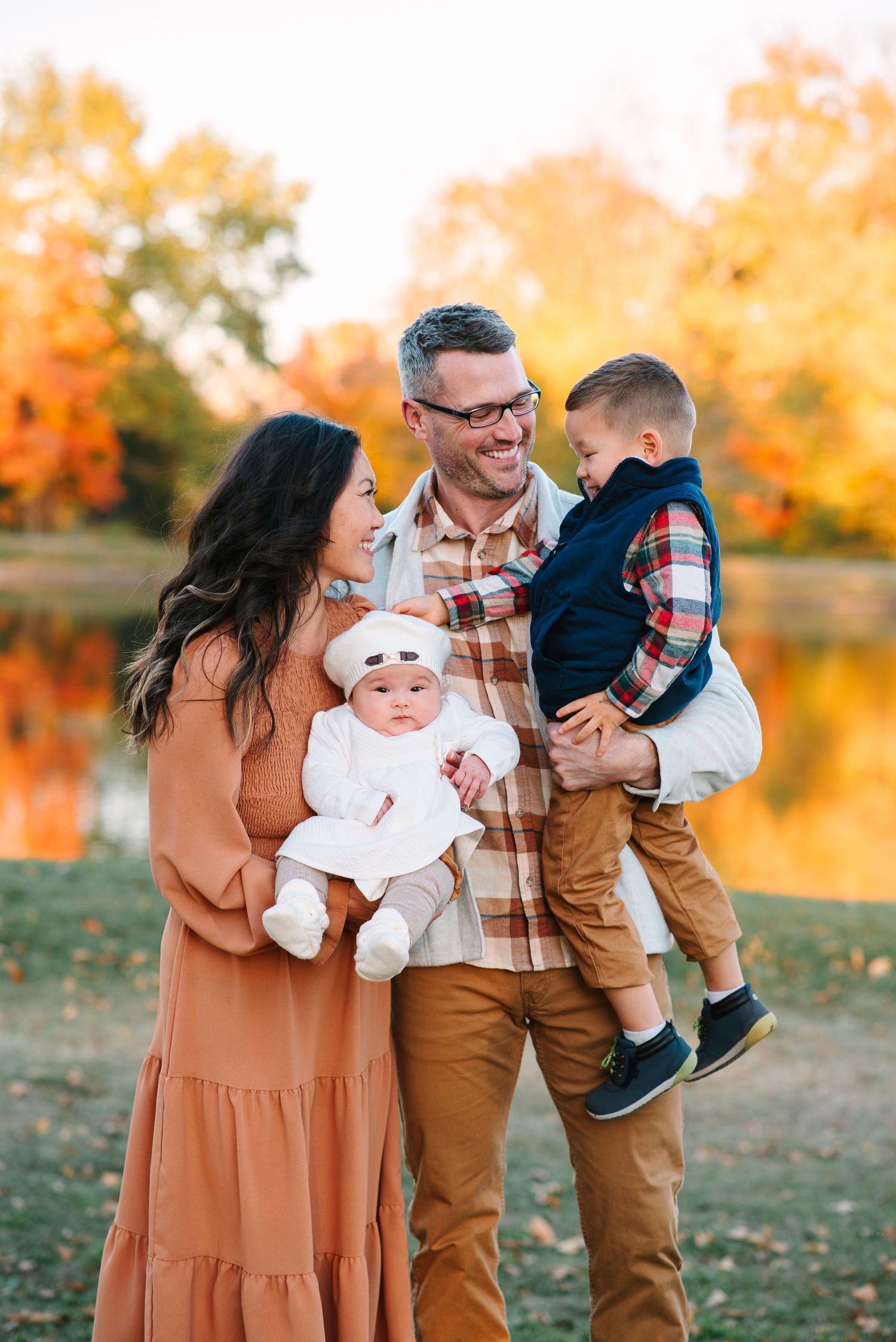 A family takes a stroll through an autumn field with their small white dog.