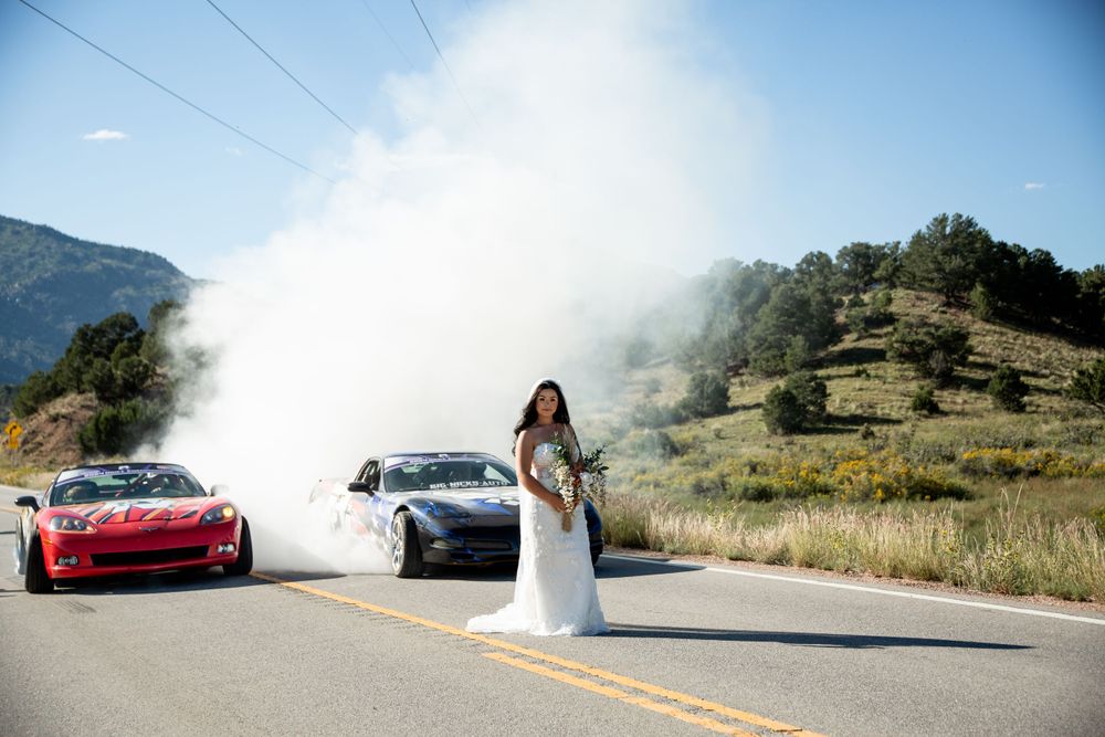 Wedding photo with sports cars creating smoke on mountain road.