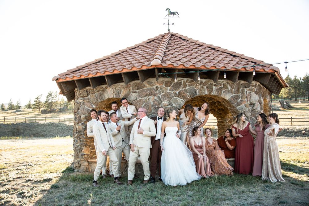 Wedding party poses together in front of a stone gazebo with the bridal party in blush and burgundy tones.