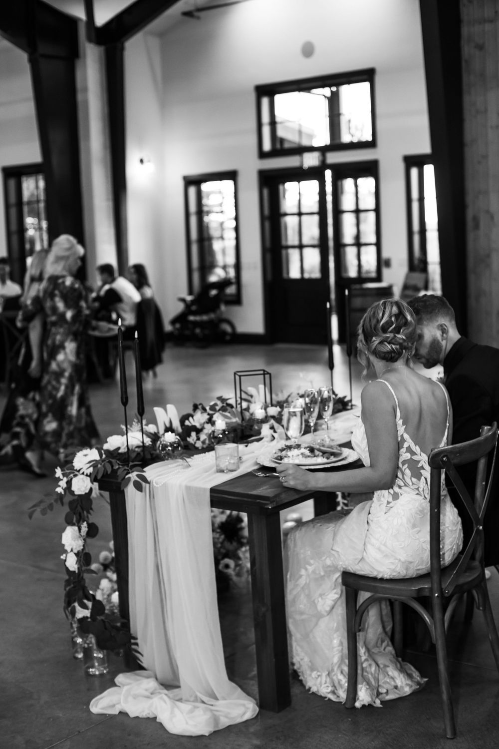 Elegant wedding reception table with floral arrangements and draped fabric in indoor venue.