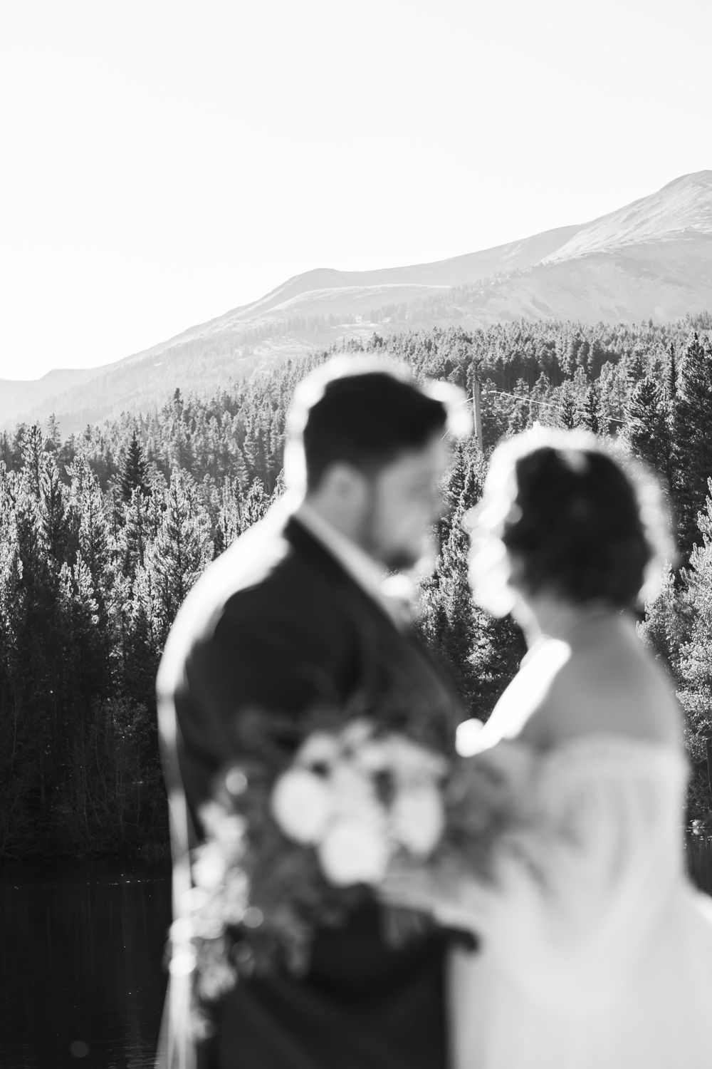 Black and white silhouette of couple with mountain forest backdrop.