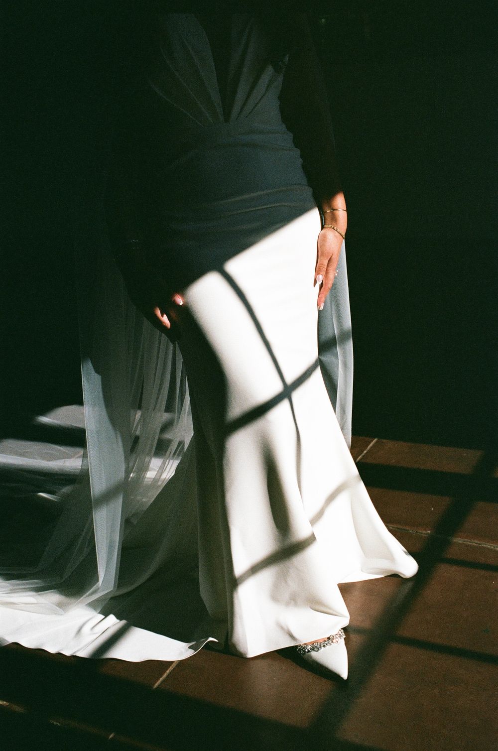 Bride in black and white wedding gown with flowing veil, dramatic shadows casting geometric patterns on dress.
