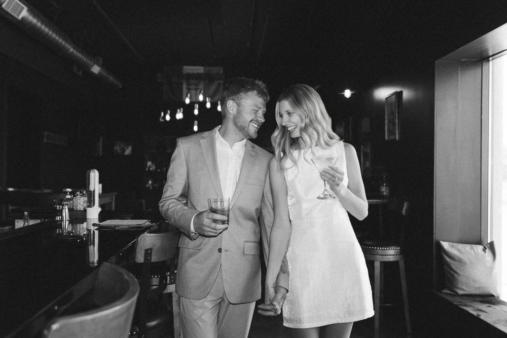 Black and white photo of a smiling couple sharing drinks in an elegant bar setting.