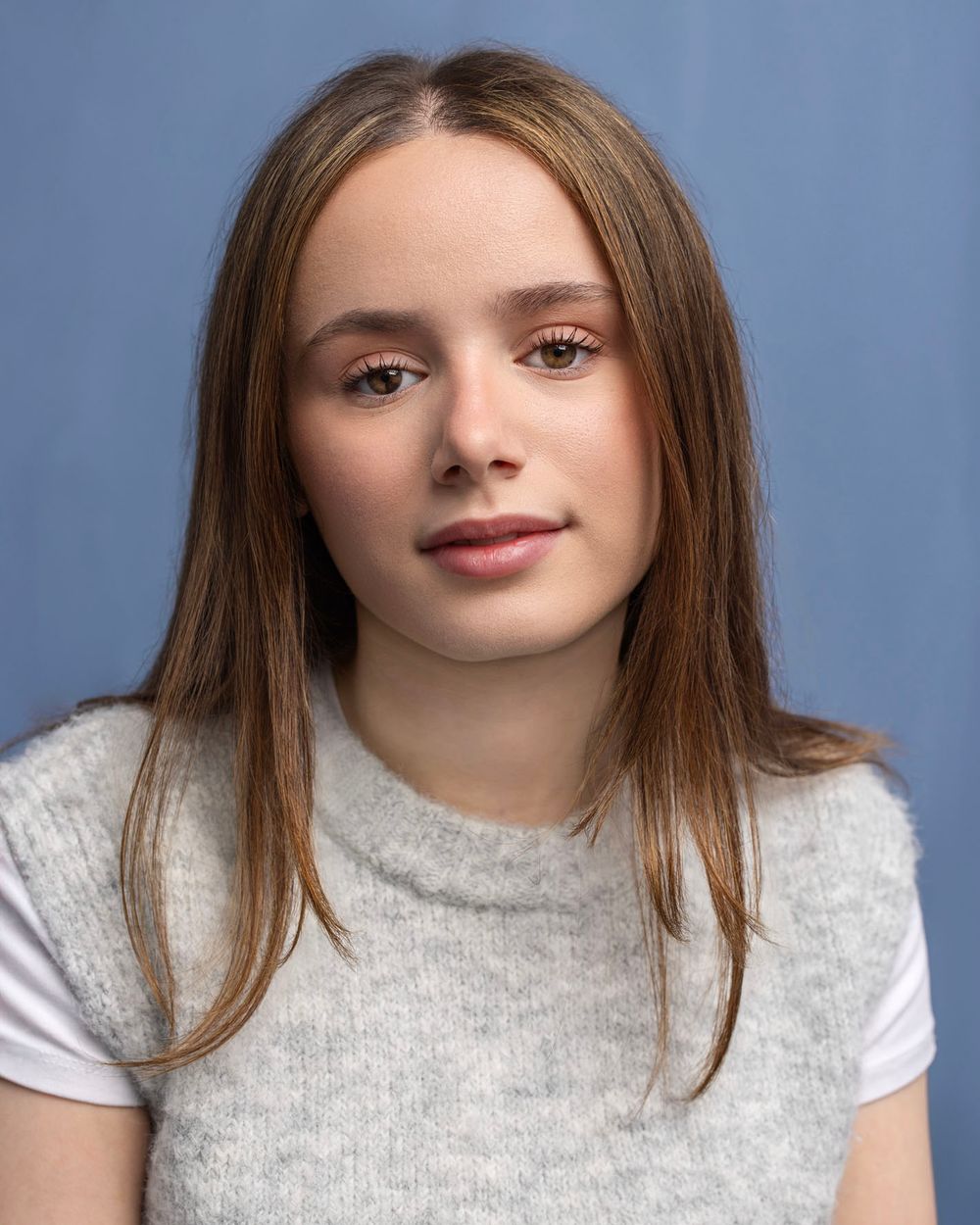 Teenage girl with shoulder-length blonde hair in grey t-shirt against blue background for young actor portfolio