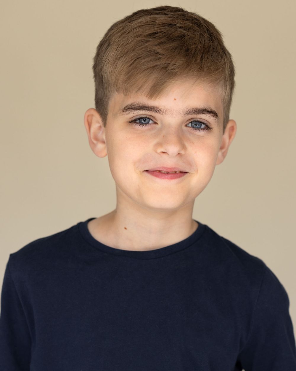 Young boy headshot wearing navy t-shirt with friendly smile for child actor portfolio against neutral backdrop