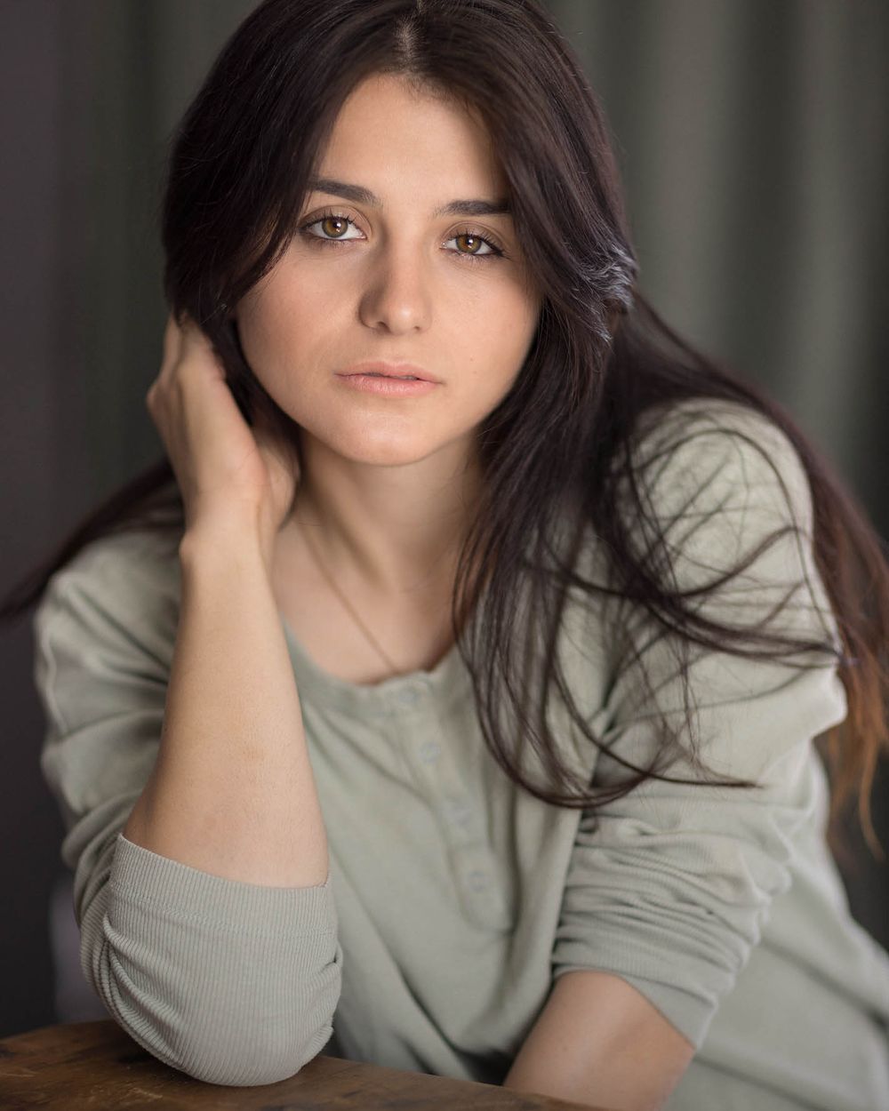 Female model portrait in sage green long-sleeve top with contemplative pose for commercial photography