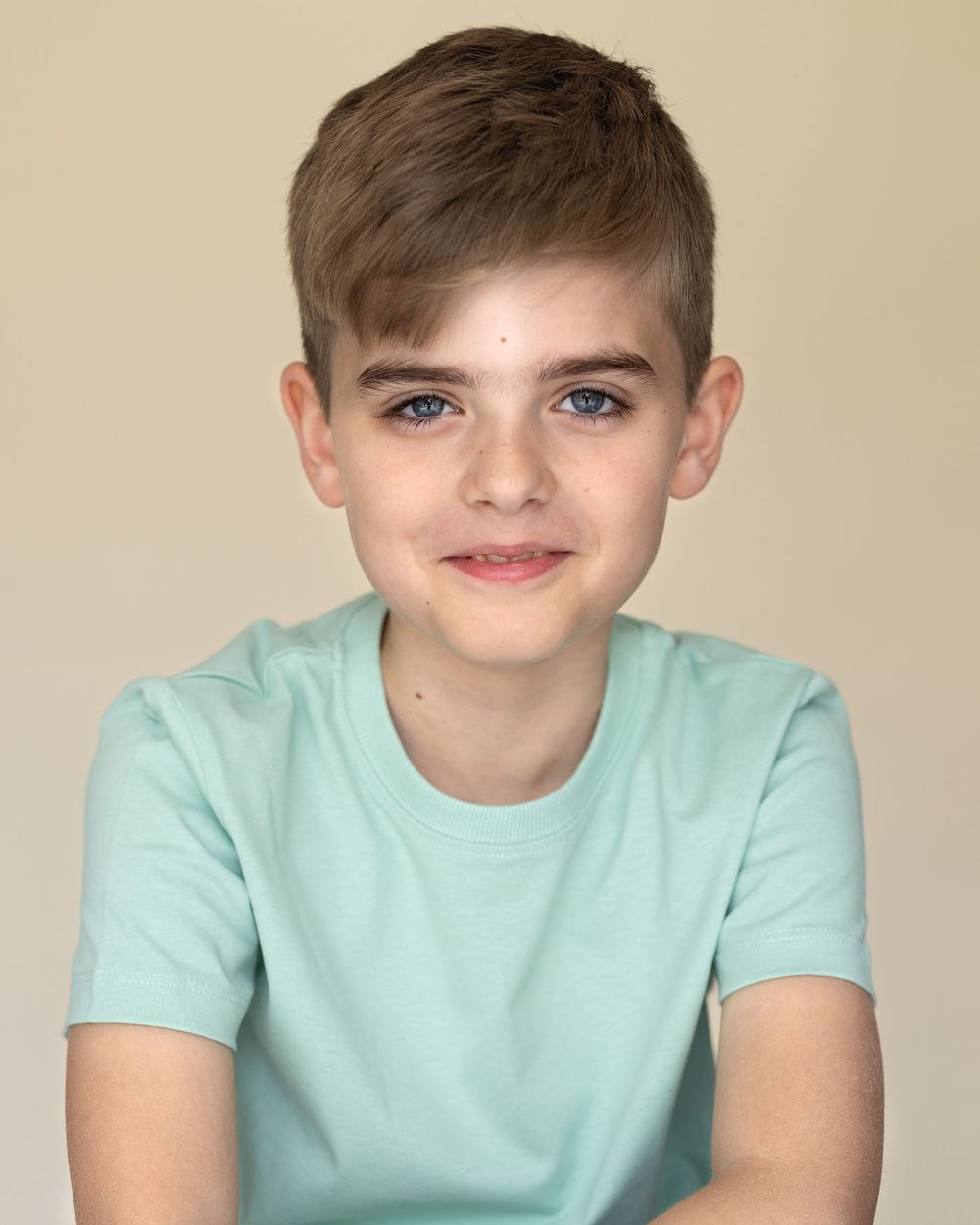 Smiling child model portrait of boy in mint green t-shirt against beige background for commercial photography