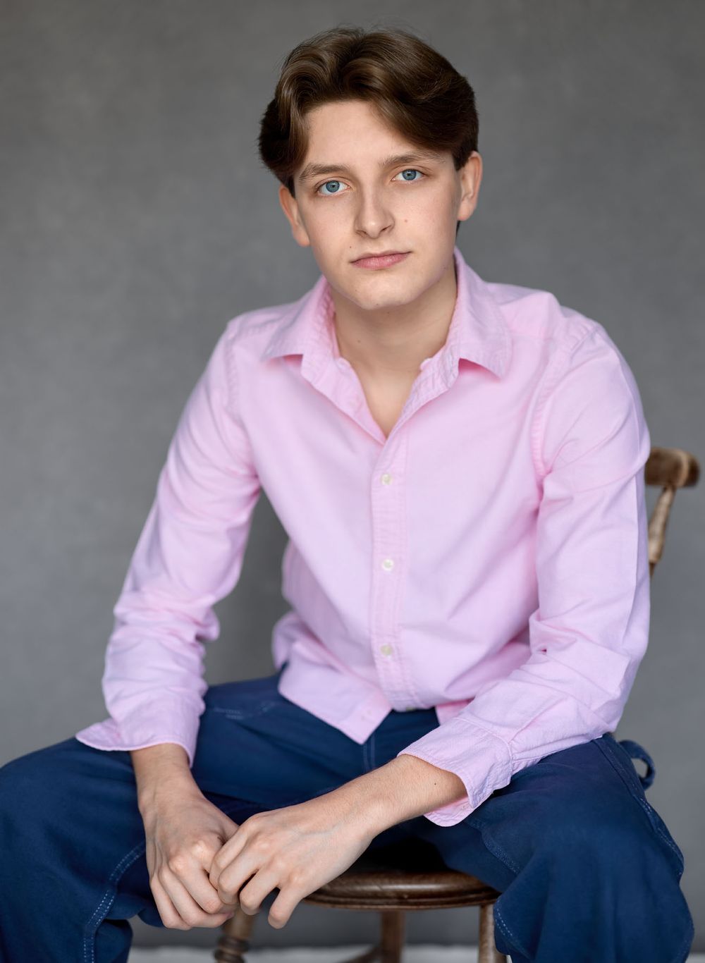 Young adult actor headshot wearing pink dress shirt and navy trousers seated for commercial portfolio photography